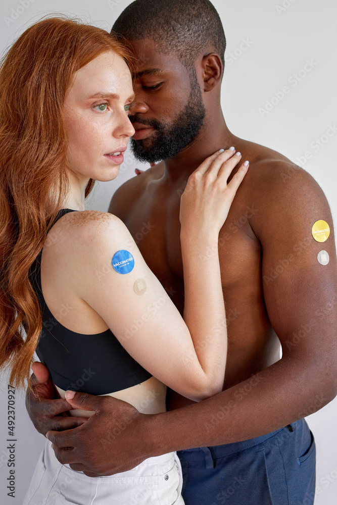 Stay at home. Young couple is vaccinated. Flu epidemic, protection against virus omicron. COVID-19, coronavirus pandemic. Portrait of shirtless black american guy and redhead caucasian lady hugging Stay at home. Young couple is vaccinated. Flu epidemic, protection against virus omicron. COVID-19, coronavirus pandemic. Portrait of shirtless black american guy and redhead caucasian lady hugging