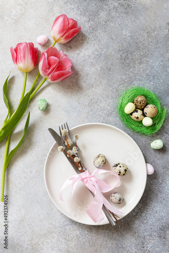 Fototapeta Naklejka Na Ścianę i Meble -  Festive Easter table setting with painted eggs, spring flowers and cutlery on light grey tabletop. Table setting for Happy Easter day.