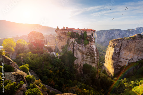 Breathtaking view of Holy Monastery of Varlaam on top of a sandstone rock with ray of light at sunrise. Must-visit iconic travel and pilgrimage destinations of the World and Greece © EdNurg