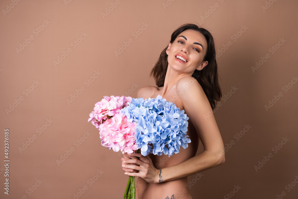 Beauty portrait of a topless woman with perfect skin and natural make-up on beige background holding bouquet of colorful flowers Beauty portrait of a topless woman with perfect skin and natural make-up on beige background holding bouquet of colorful flowers