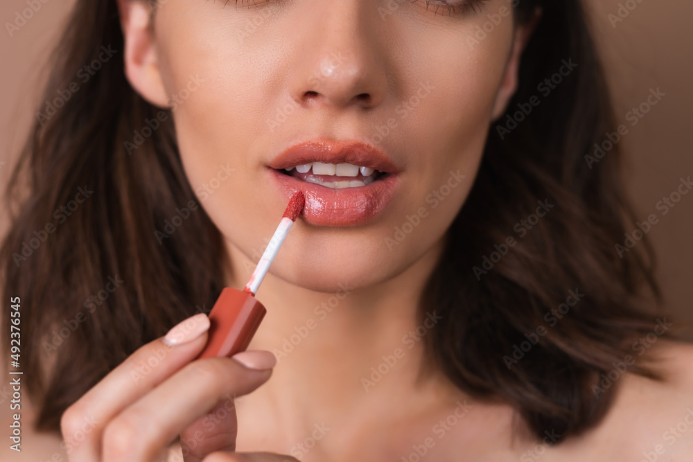 Beauty portrait of topless woman with perfect skin and natural make-up on beige background holding brown chocolate gloss lipstick Beauty portrait of topless woman with perfect skin and natural make-up on beige background holding brown chocolate gloss lipstick