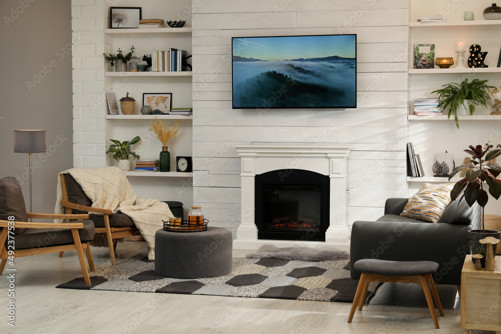 Fototapeta premium Cozy living room interior with comfortable sofa, armchairs and decorative fireplace