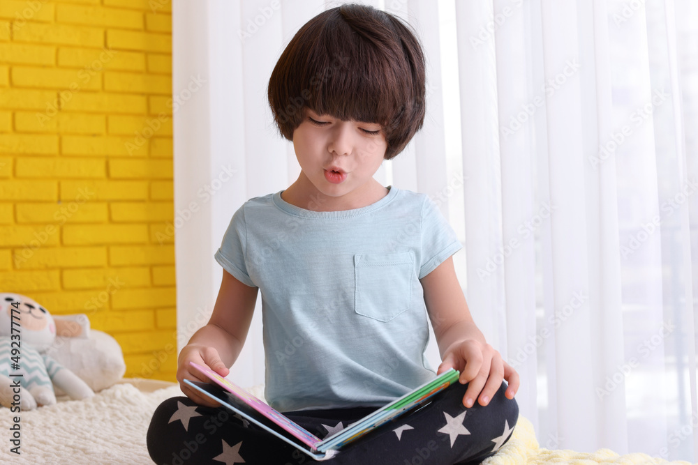 Cute little boy reading book on bed at home Cute little boy reading book on bed at home