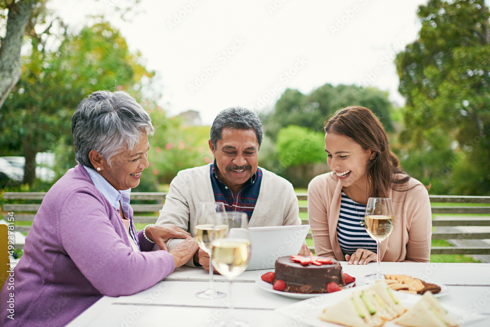 Lets post this birthday selfie on social media. Cropped shot of a senior man showing his family something on his tablet as they have lunch outside.