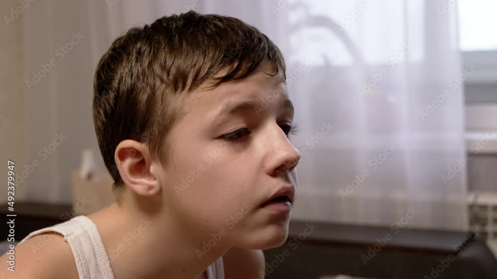A Face of a Serious Child, Carefully Looking at the Monitor Screen. Side View. Profile of a focused teenager sitting in a room and studying, reading information from the TV screen. Home atmosphere. A Face of a Serious Child, Carefully Looking at the Monitor Screen. Side View. Profile of a focused teenager sitting in a room and studying, reading information from the TV screen. Home atmosphere.