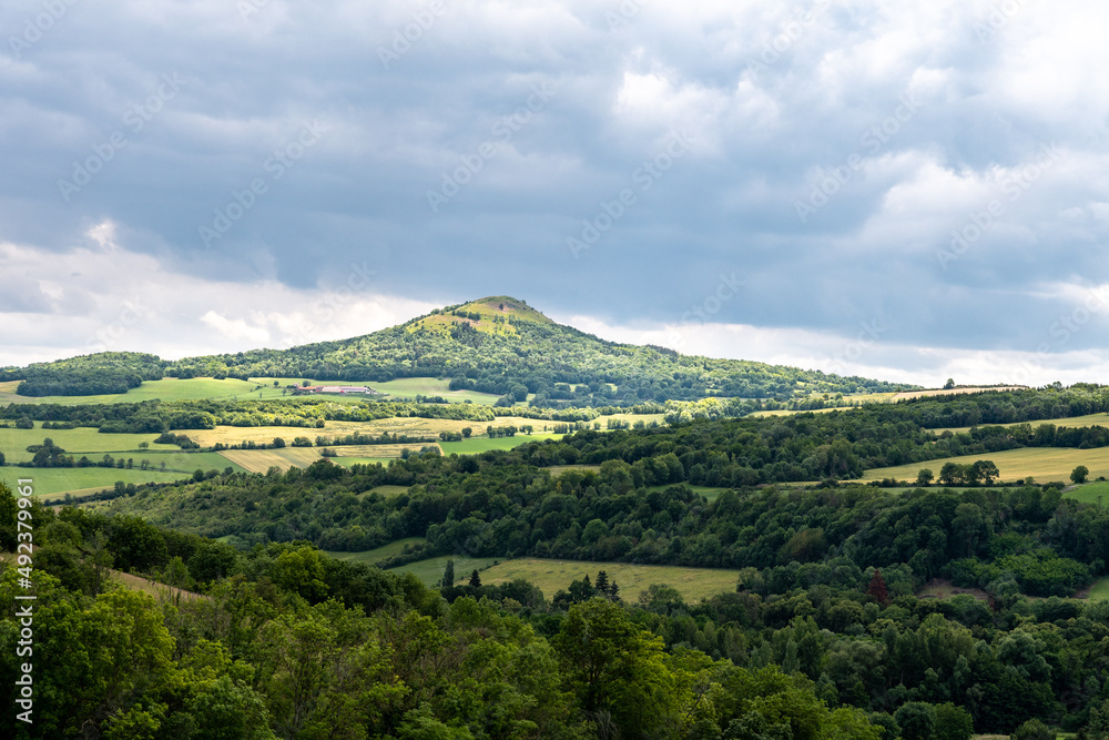 vue sur un volcan tronant au mileu d'une vallée sur le chemin de randonnée du puy de Lavelle dans le puy de dôme avec ses pentes boisées et son sommet en herbes