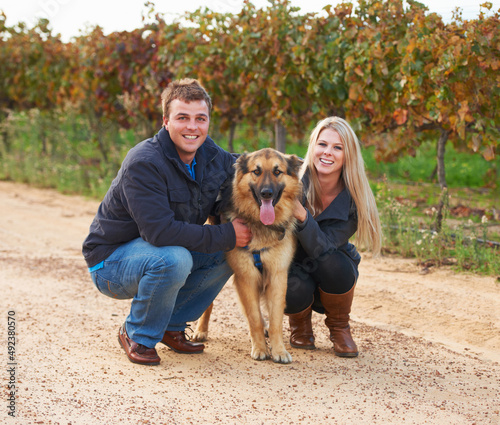 Hes a member of their family. Portrait of a young couple with their pet Alsatian on a wine farm.