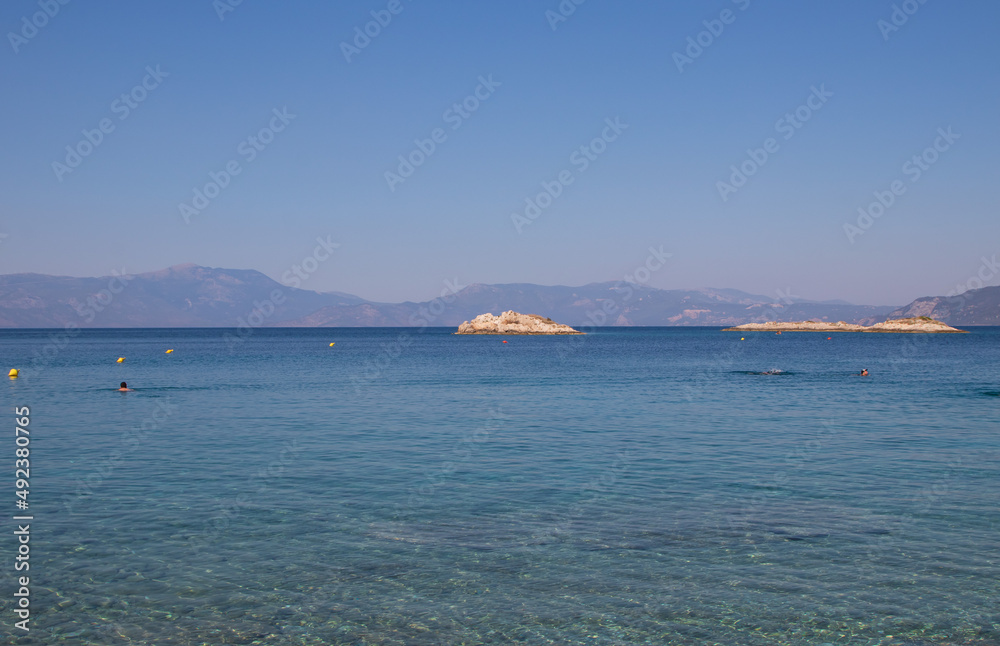 Seascape, greek beach with clear mediterranean sea, bathing people and small island, Greece