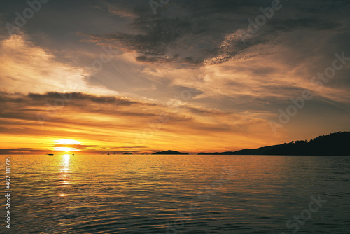 Dramatic sunset over sea with clouds in the sky and mountain in background - Thailand Koh Lipe