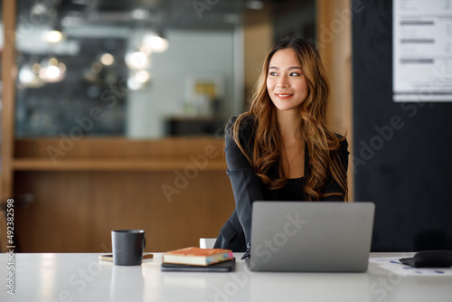 Charming Asian businesswoman sitting in the office with a digital laptop computer. Excited Asian businesswoman raising hands to congratulate while working in a modern office,