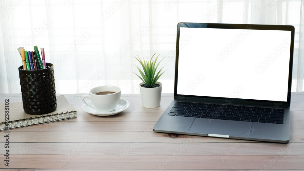 Fototapeta premium Work form home or online learning concept on wooden table desk with blank screen laptop computer and coffee cup, stationery, social distance during quarantine, self-isolation, online education concept