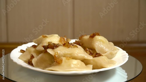 Ukrainian dumplings with fried onions on a plate. Continuous rotation on a movable stand. Fresh homemade dish. Seamless video