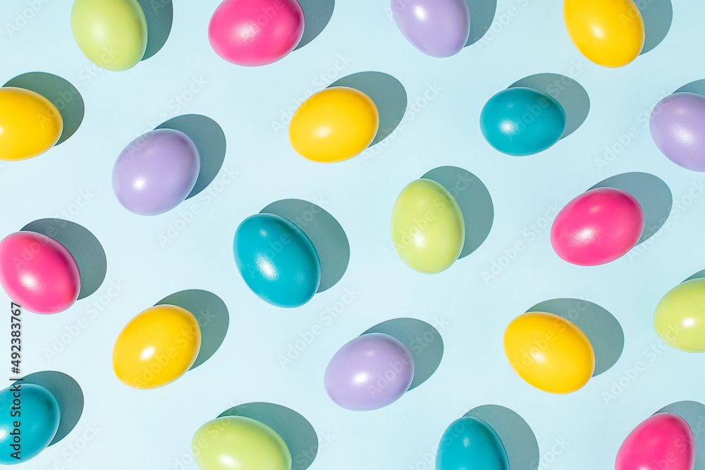 Colorful pattern made of Easter eggs on pastel blue background. Creative holiday wallpaper concept. Minimal top view flat lay composition.