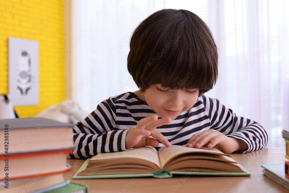 Cute little boy reading book at table in room Cute little boy reading book at table in room