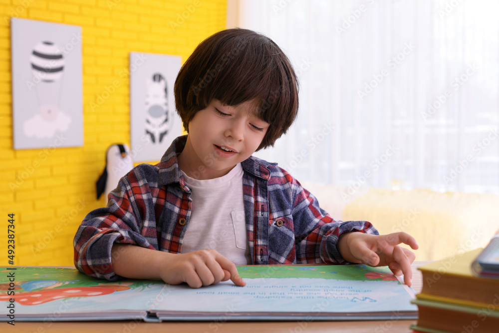 Cute little boy reading book at table in room Cute little boy reading book at table in room