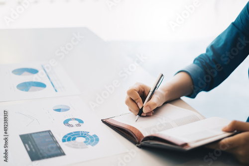 Asian Business Woman or Accountant hands holding pen writing in notebook with paperwork, account, audit and saving concept.