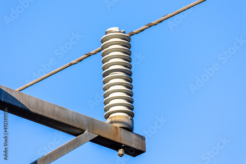 close up of ceramic isolator and wire cable on an electrical pylon. Blue neutral sky background