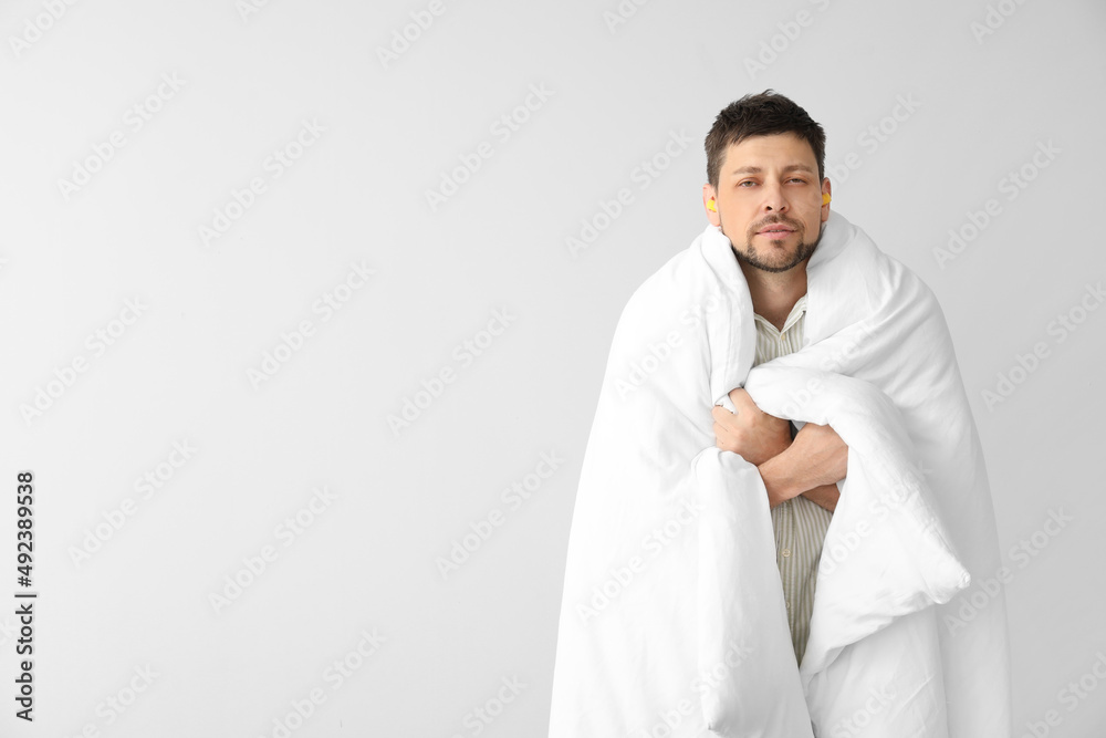 Handsome man with ear plugs and blanket on light background