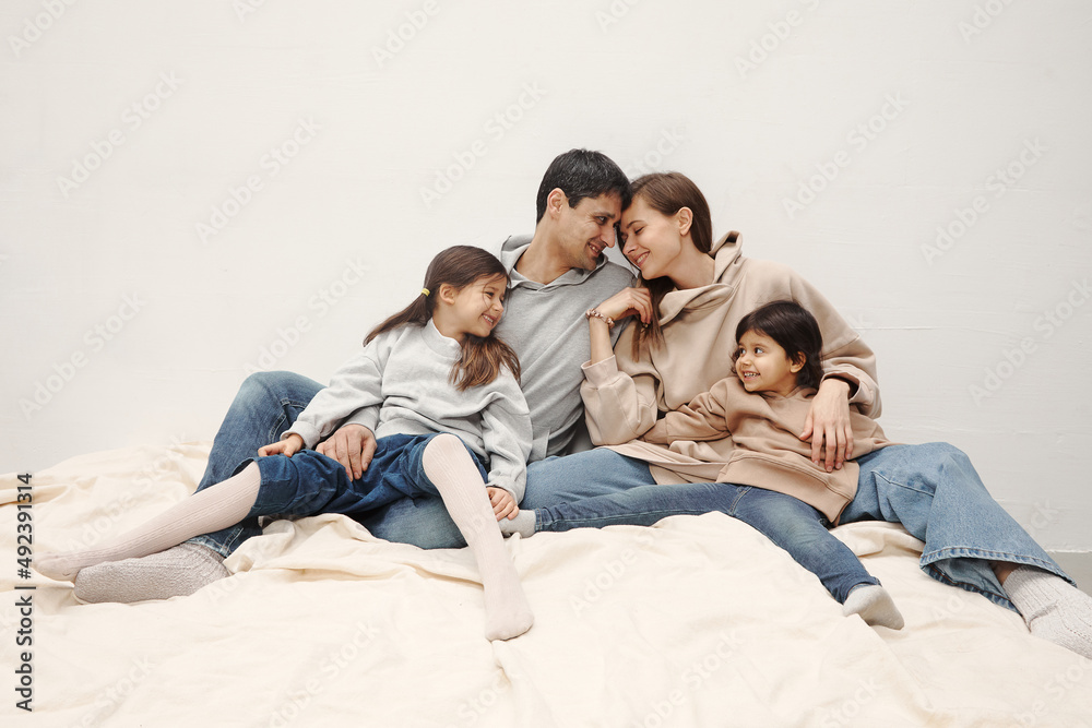 Portrait of happy caucasian parents posing with their little daughters at home, beige pastel background