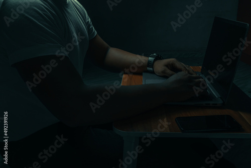 A man in a white shirt sits on a laptop in a dark room. with light shining down. internet concept addiction.topview.