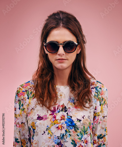 Stunning and stylish. Portrait of an attractive young woman wearing designer shades against a pink background.