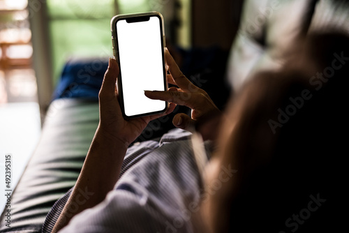 Woman resting on couch using with white Mock-up screen smartphone. Young woman using Mobile phone in vertical mode, Internet browsing, posting on social networks