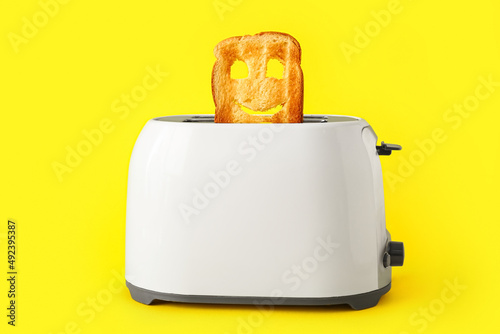 Funny slice of bread in toaster on yellow background