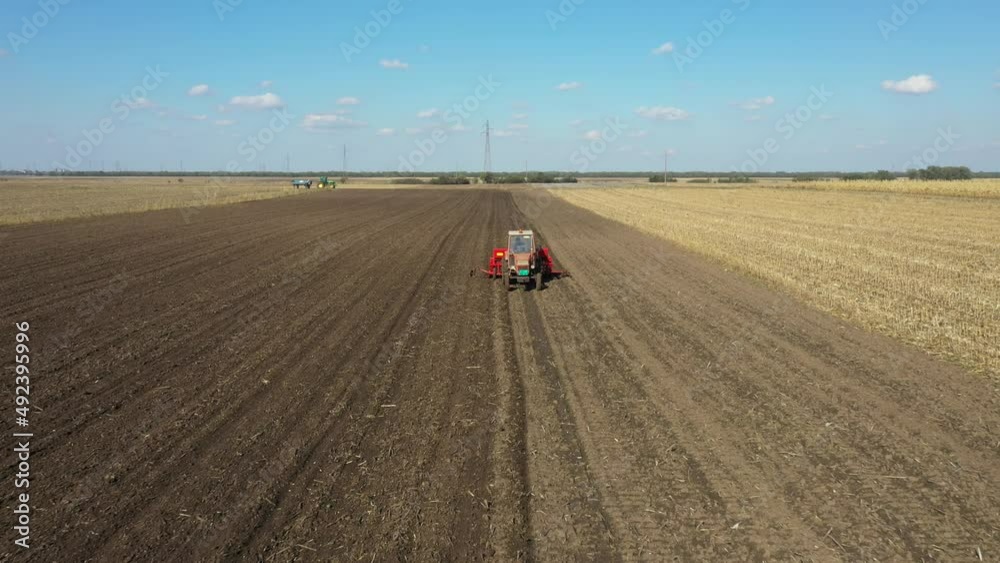 Above dolly move, flying over in backwards, tractor is pulling seed drill machine over arable field, soil, planting new wheat crop. Above dolly move, flying over in backwards, tractor is pulling seed drill machine over arable field, soil, planting new wheat crop.