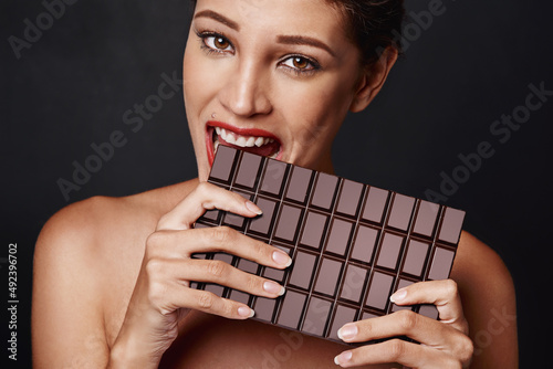 Yes, size matters. Studio shot of an attractive young woman biting into a slab of chocolate.