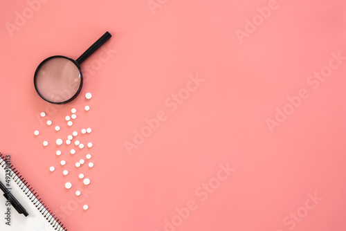 Flat lay, pills and magnifier on pink background, copy space. photo