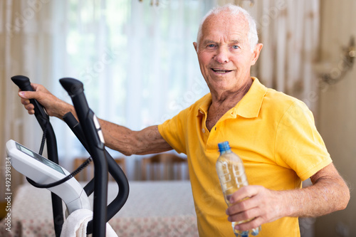 Man with bottle of water training with cross-trainer