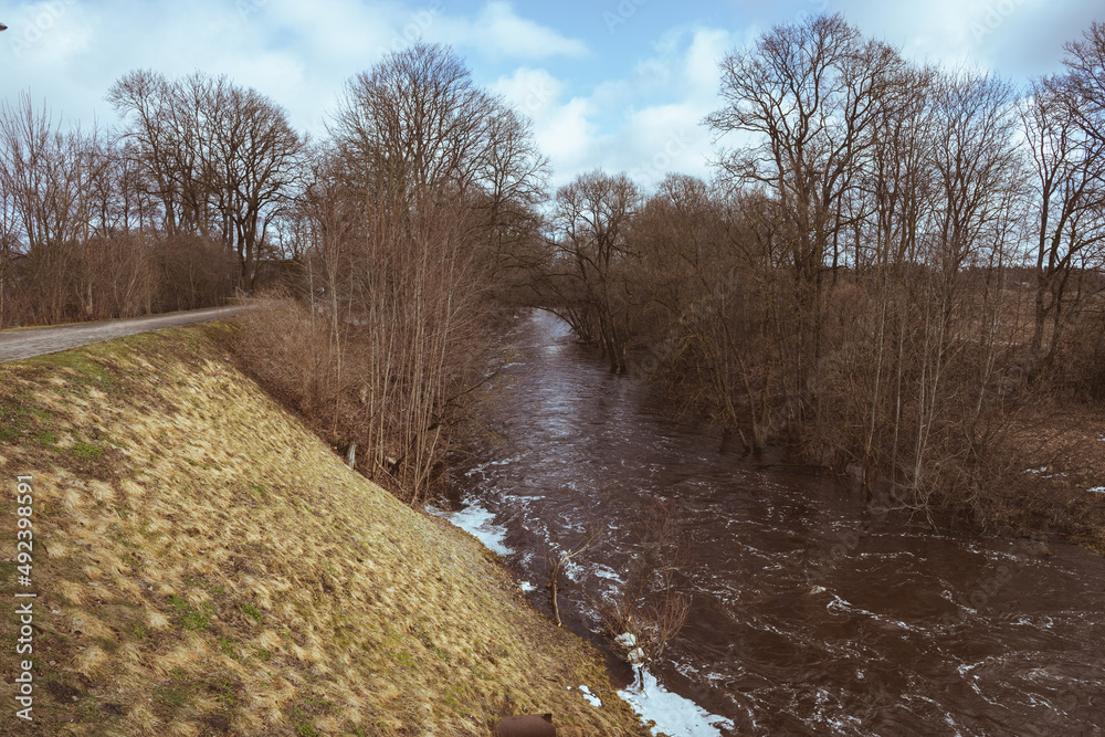 rapid river in valley, bare trees, walkway on riverside