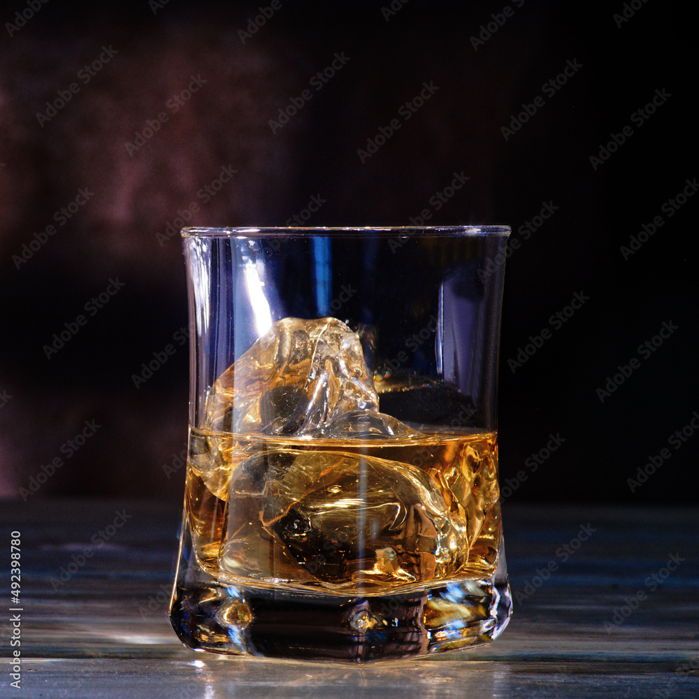 Glass of amber scotch whiskey and ice on a dark background