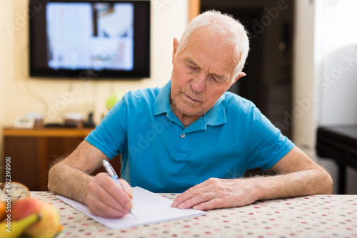 Focused senior man reading and signing papers at home table