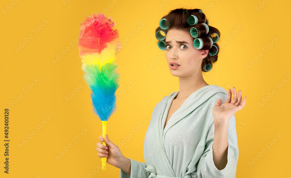 Confused Lady With Hair Curlers Holding Feather Duster, Yellow Background