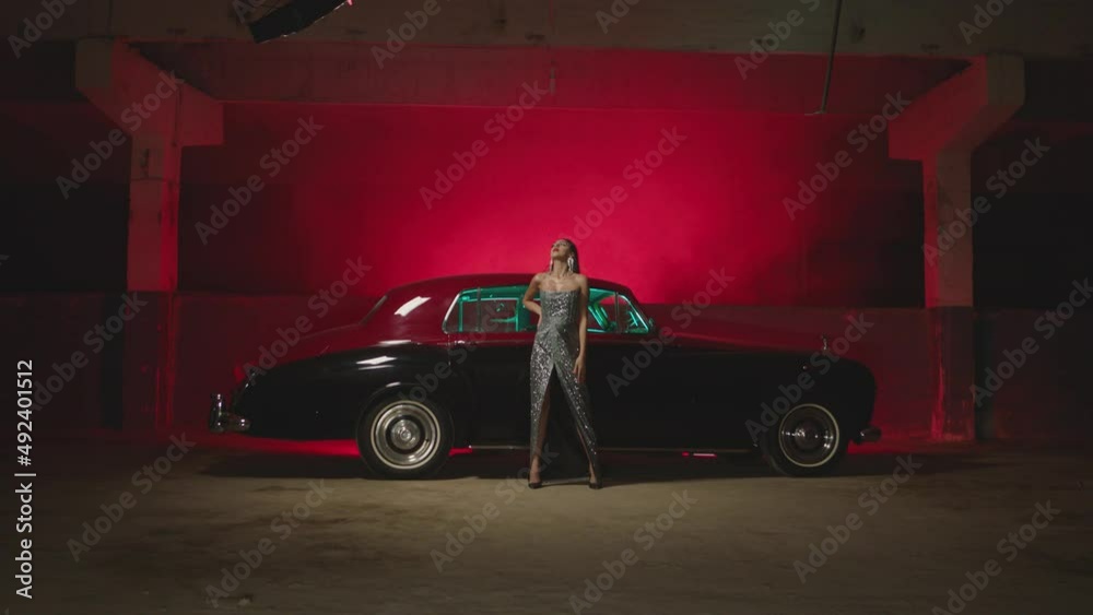 Beautiful Elegant Young Woman Standing , Dancing and Flirting near old retro classic car. Old fashioned luxury style concept . Rich fashion lifestyle . Luxury dress with fabric glitter, spangles .