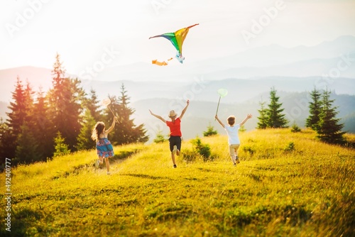 Three kids in the mountains at sunset play kite and butterfly fishing net. Happy summer holidays and childhood.