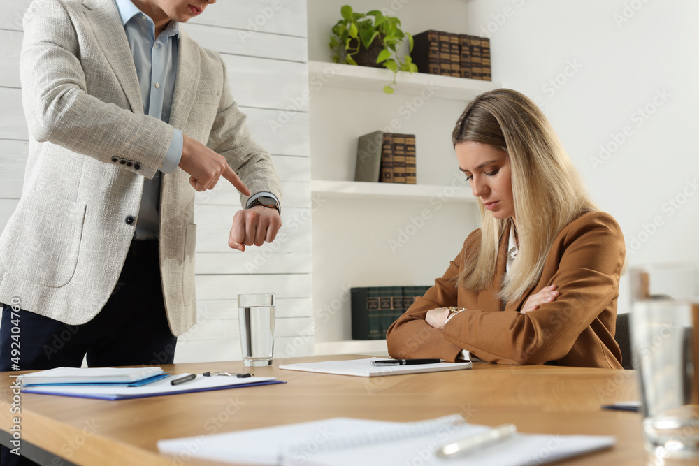 Businessman pointing on wrist watch while scolding employee for being late in office Businessman pointing on wrist watch while scolding employee for being late in office