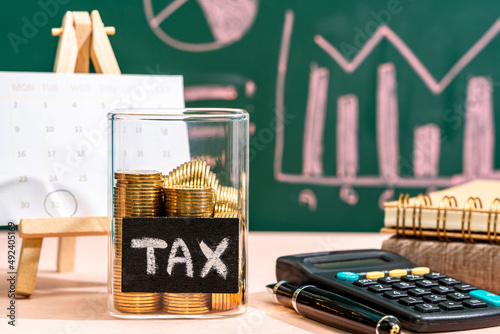 Many gold coins were put in a glass jar and wooden signs with tax messages, Next comes a calculator and an account book. Calculating annual income tax returns for government sectors concept.