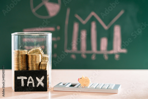 Many gold coins were put in a glass jar and wooden signs with tax messages and pig model placed on a calculator. Annual income tax return to the government sector concept.