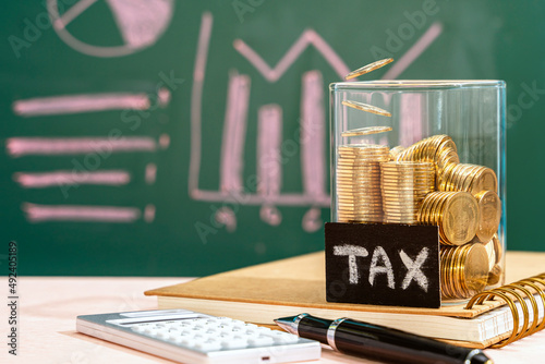 Many gold coins were put in a glass jar and wooden signs with tax messages, Next comes a calculator and an account book. Calculating annual income tax returns for government sectors concept.