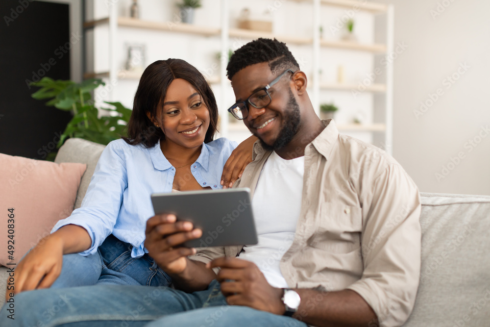 Lovely African American couple sitting on sofa, using tablet Lovely African American couple sitting on sofa, using tablet