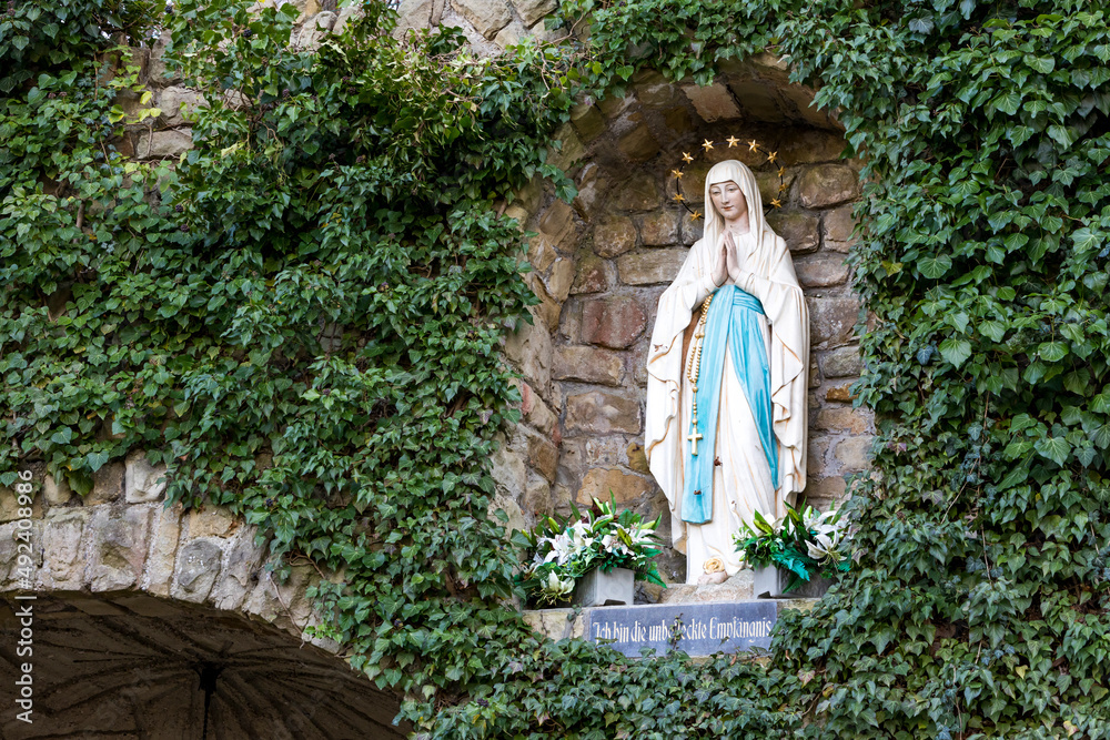 Statue der Gottesmutter Maria umrahmt von Efeu