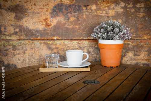 white coffee cup and glass of water on vintage wooden table and flower pot