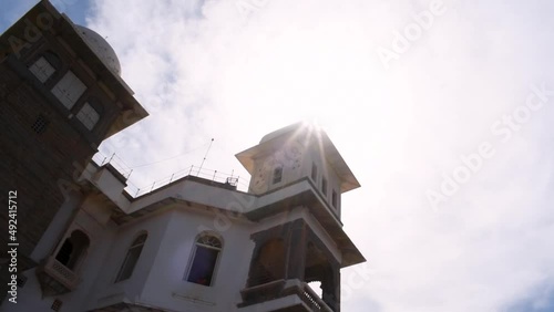 The Monsoon Palace or Sajjan Garh Palace in background of cloudy sky with sun star. At Udaipur, Rajasthan, India. White color Indian old palace under sunny sky. Historic travel destination in India photo