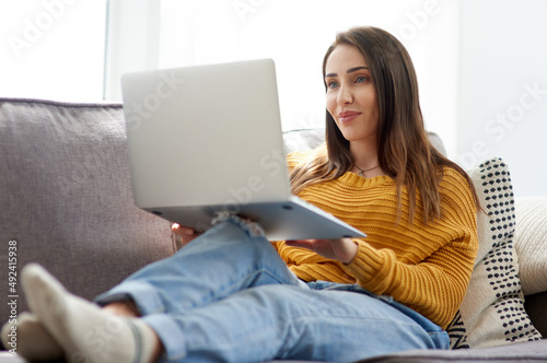 Spending the day streaming all the shows she wants. Shot of a young woman using a laptop while relaxing on a sofa at home.