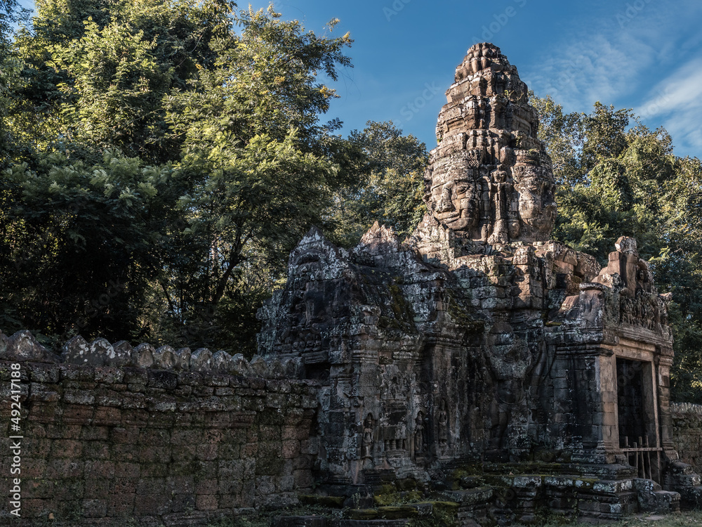 Ancient stone wall and entrance tower with sacred faces in Angkor complex, Siem Reap, Cambodia