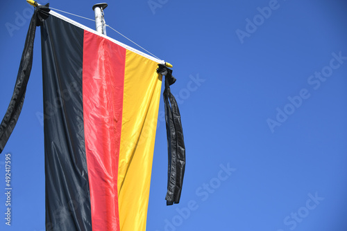 Die Nationalfahne der Bundesrepublik Deutschland schwarz, rot, gold, hängt am Fahnenmast. Als Symbol der Staatstrauer ist der Trauerflor mit zwei schwarzen Schleifen an der Fahne angehängt. 