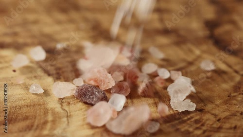 Pink Himalayan rock salt passes in front of the camera on a wooden cutting board  photo