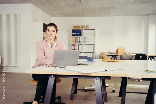 woman in a spacious bright office, at a desk with a laptop. she looks at the camera © contrastwerkstatt